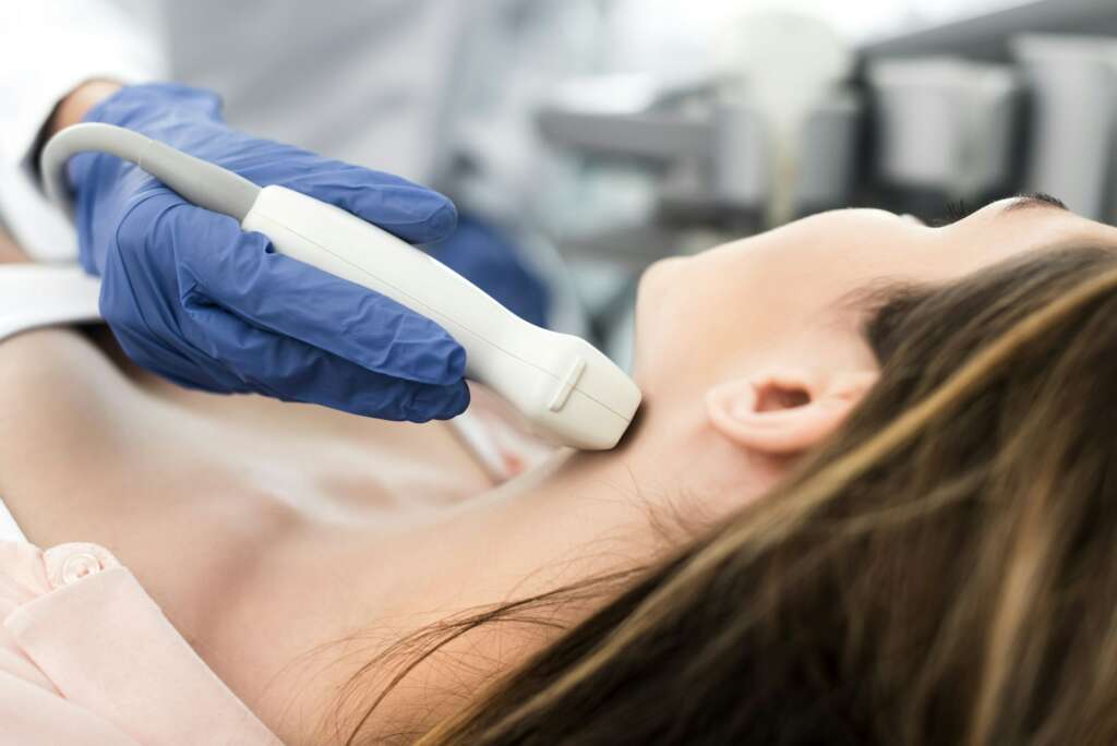 doctor examining thyroid of female patient with ultrasound scan in clinic