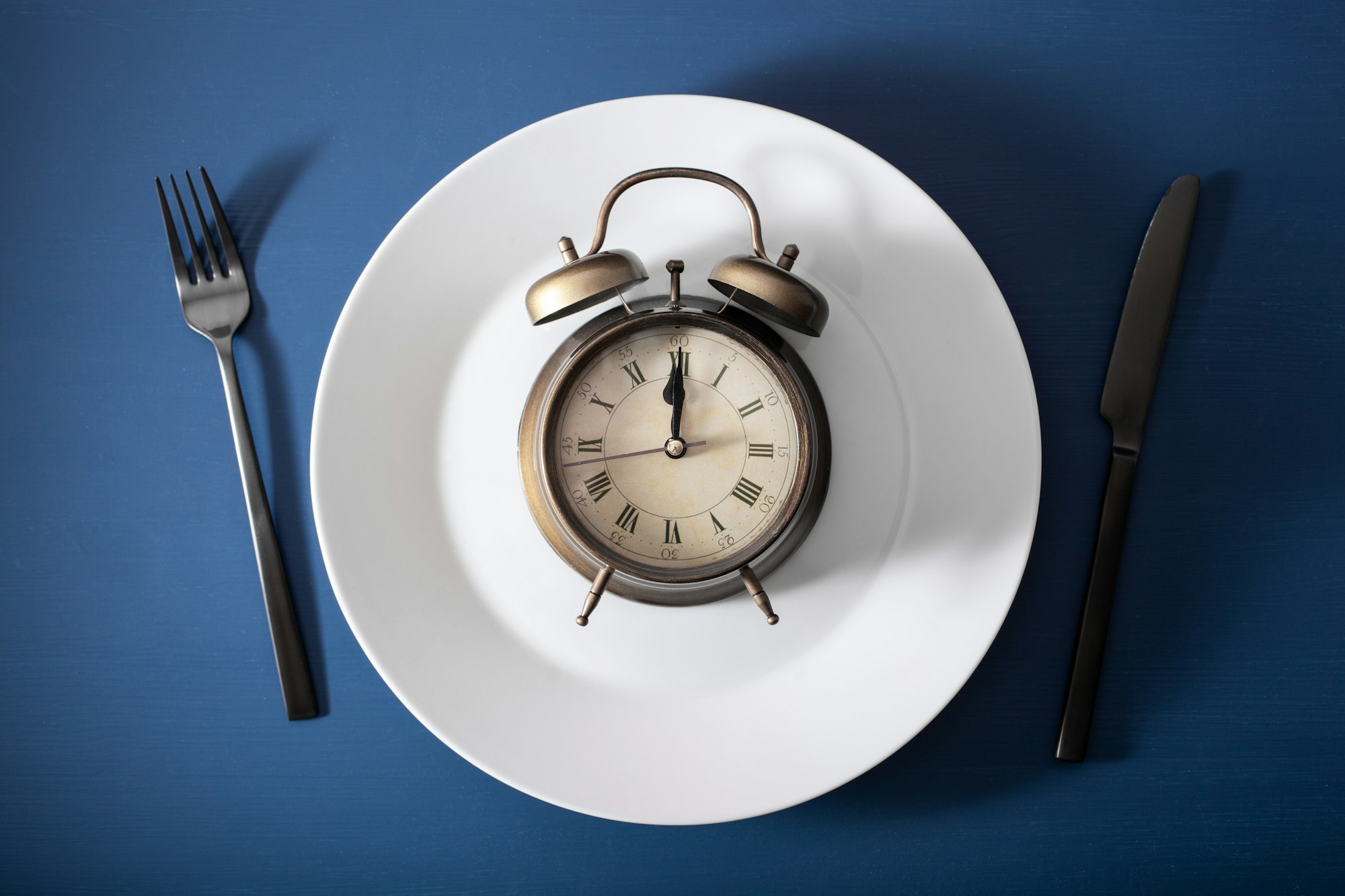 concept of intermittent fasting, ketogenic diet, weight loss. fork and knife, alarmclock on plate