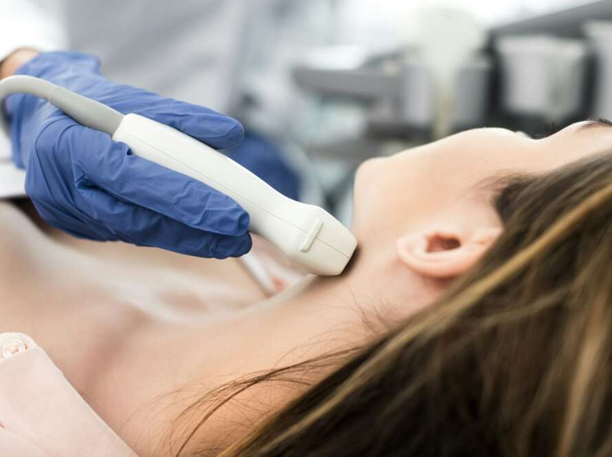 doctor examining thyroid of female patient with ultrasound scan in clinic