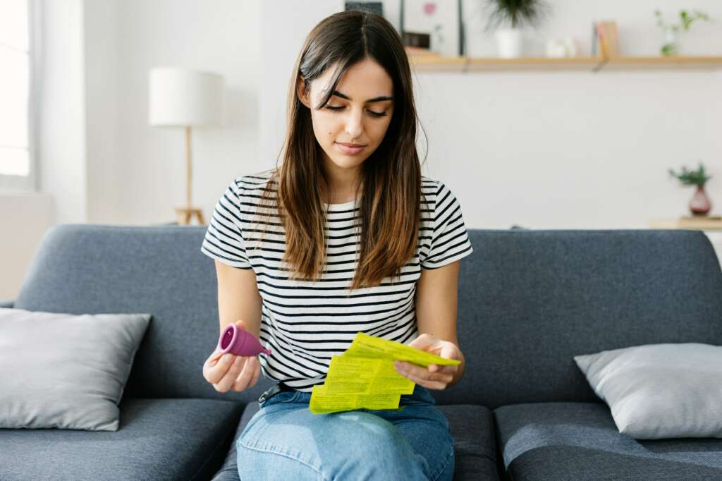 Young woman reading silicone menstrual cup use instructions at home.